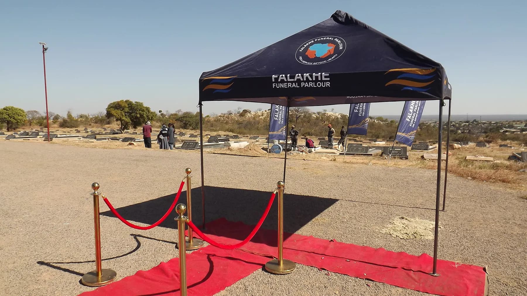 A Falakhe gazebo with a red carpet and gold rope stands at the graveside